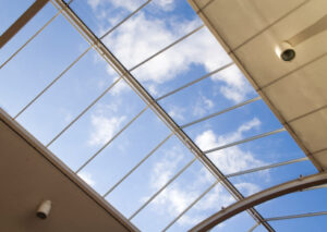 Glass roof seen from below, blue sky with drifting clouds visible